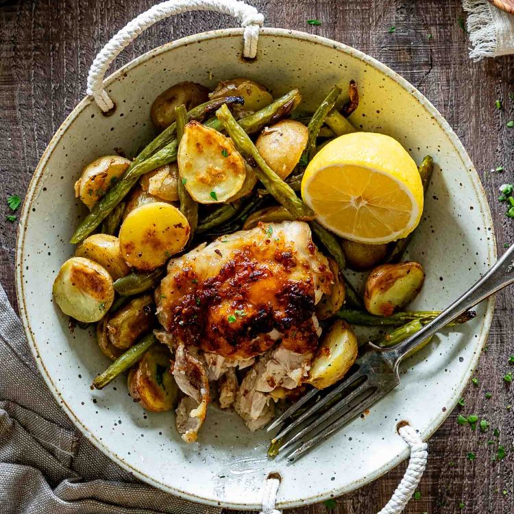 Rustic bowl filled with Parmesan garlic chicken, roasted baby potatoes, green beans, and fresh lemon on wooden table.