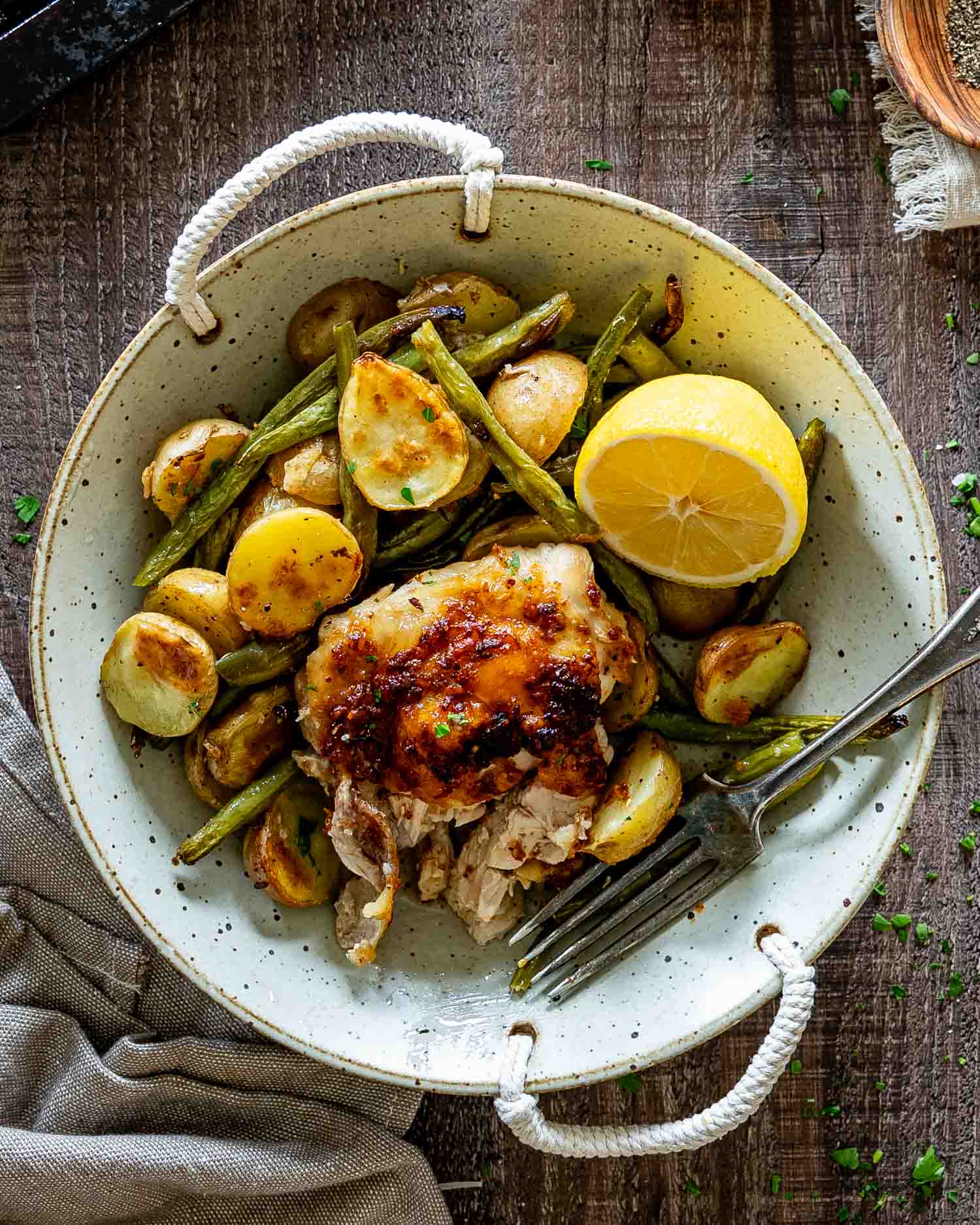Rustic bowl filled with Parmesan garlic chicken, roasted baby potatoes, green beans, and fresh lemon on wooden table.