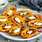 A full plate of crispy restaurant style potato skins loaded with melted cheddar cheese, crumbled bacon, green onions, and dollops of sour cream.