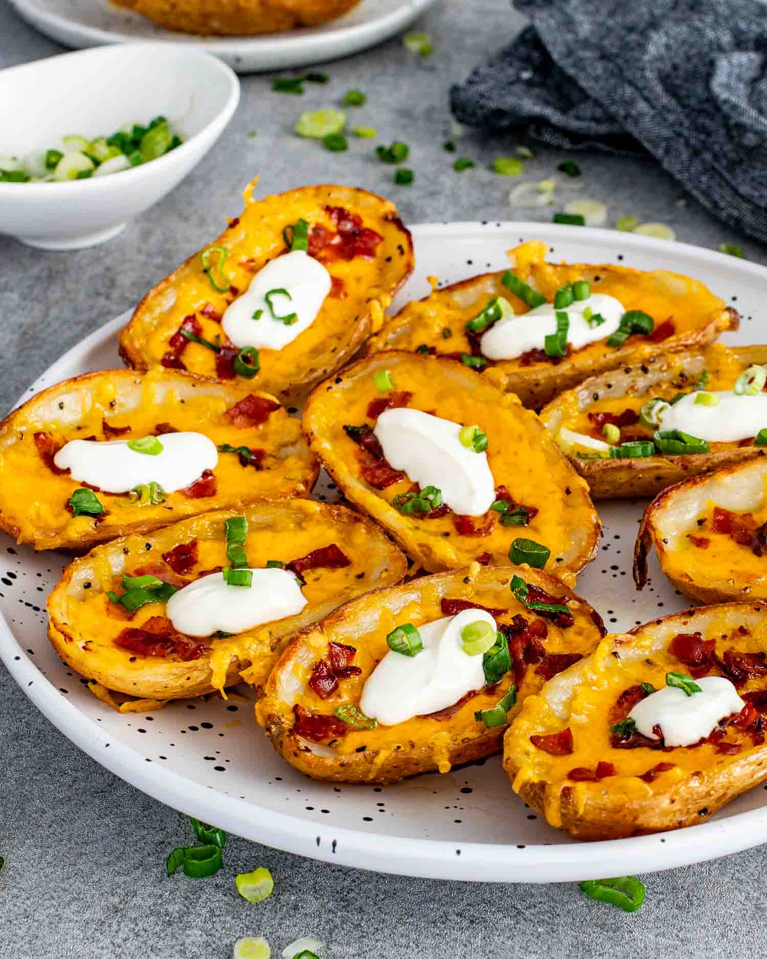 A full plate of crispy restaurant style potato skins loaded with melted cheddar cheese, crumbled bacon, green onions, and dollops of sour cream.