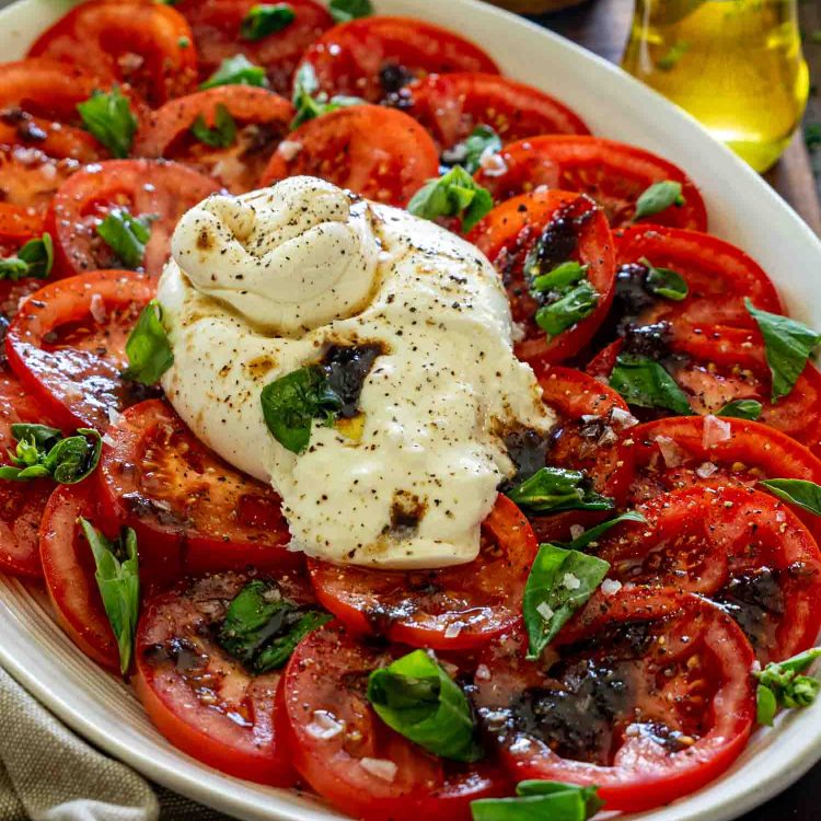 Close up tomato burrata salad with creamy burrata, fresh basil, balsamic glaze, olive oil, and sliced ripe tomatoes.