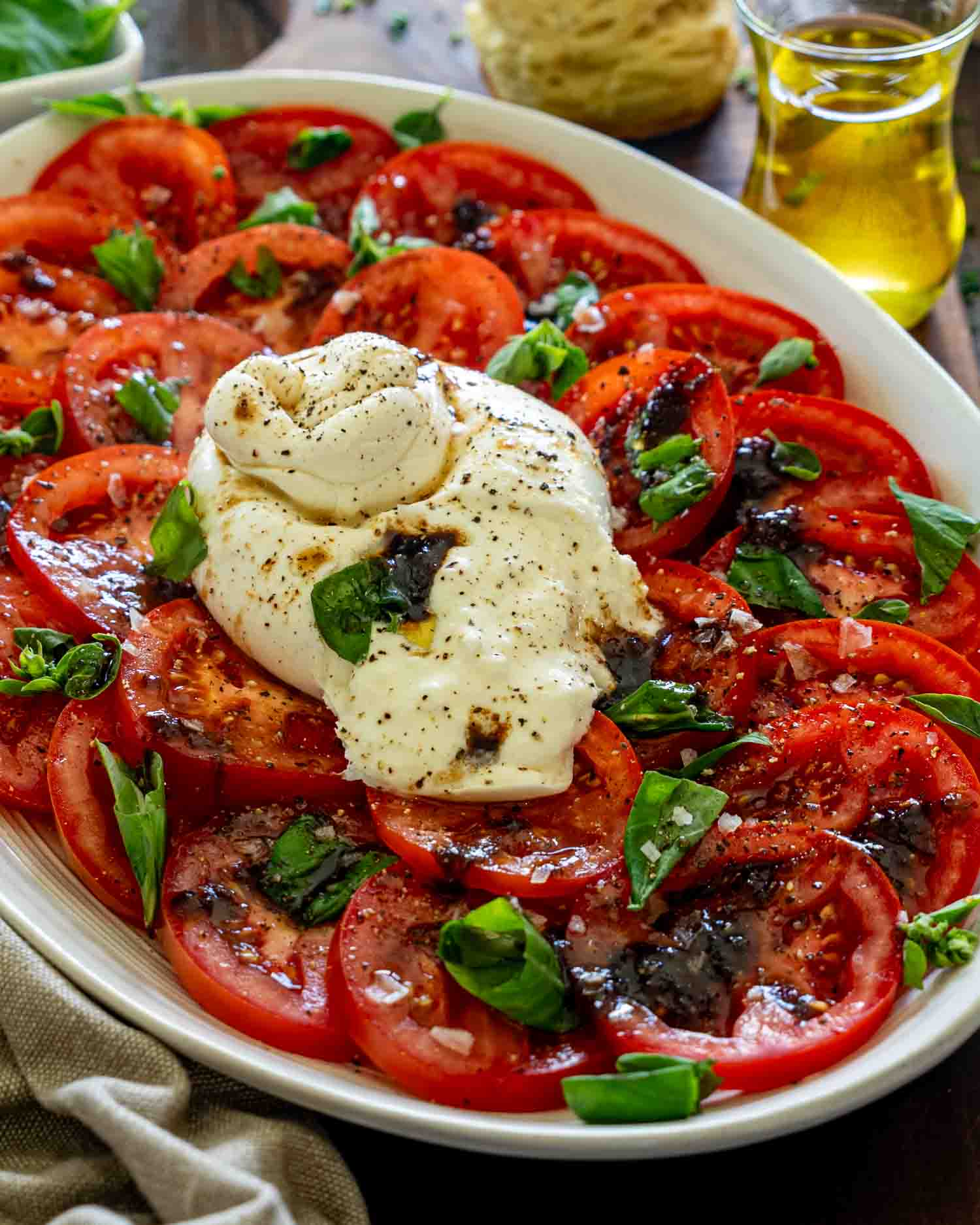 Close up tomato burrata salad with creamy burrata, fresh basil, balsamic glaze, olive oil, and sliced ripe tomatoes.