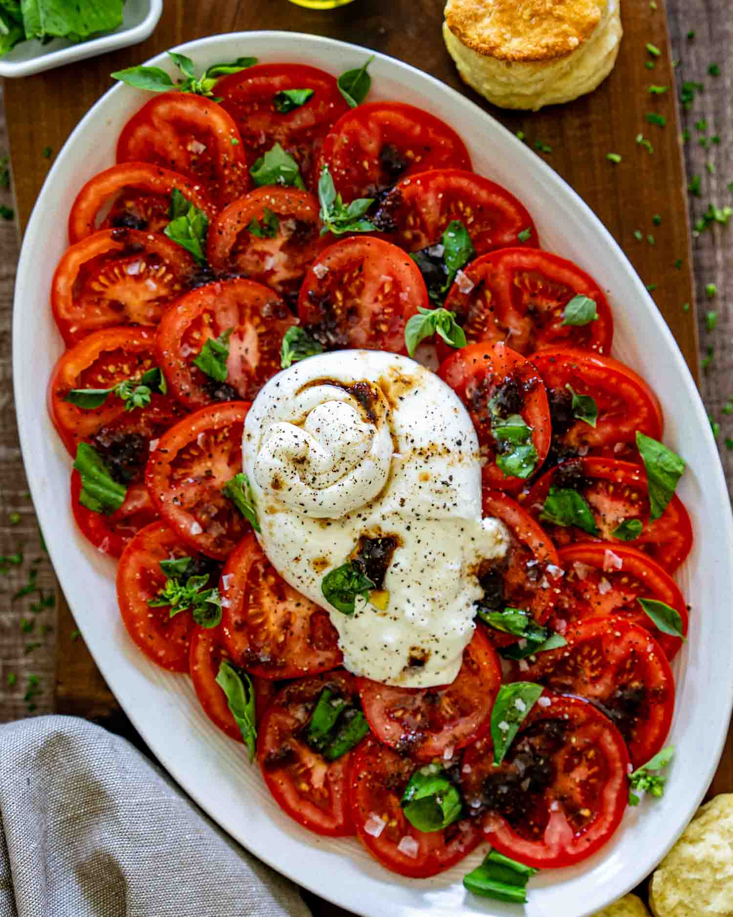 Rustic tomato burrata salad topped with fresh basil, cracked pepper, balsamic glaze, and creamy burrata cheese on platter.