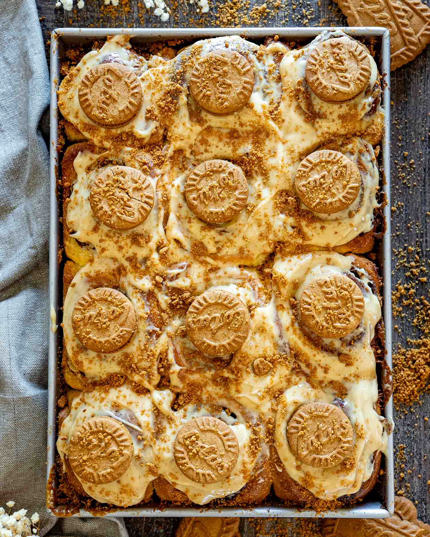 Overhead view of Biscoff cinnamon rolls baked together in a pan with creamy frosting, crushed cookies, and whole Biscoff biscuits.