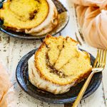 Thick slice of cinnamon roll cream cheese pound cake topped with cream cheese glaze, served on a black plate with a gold dessert fork.