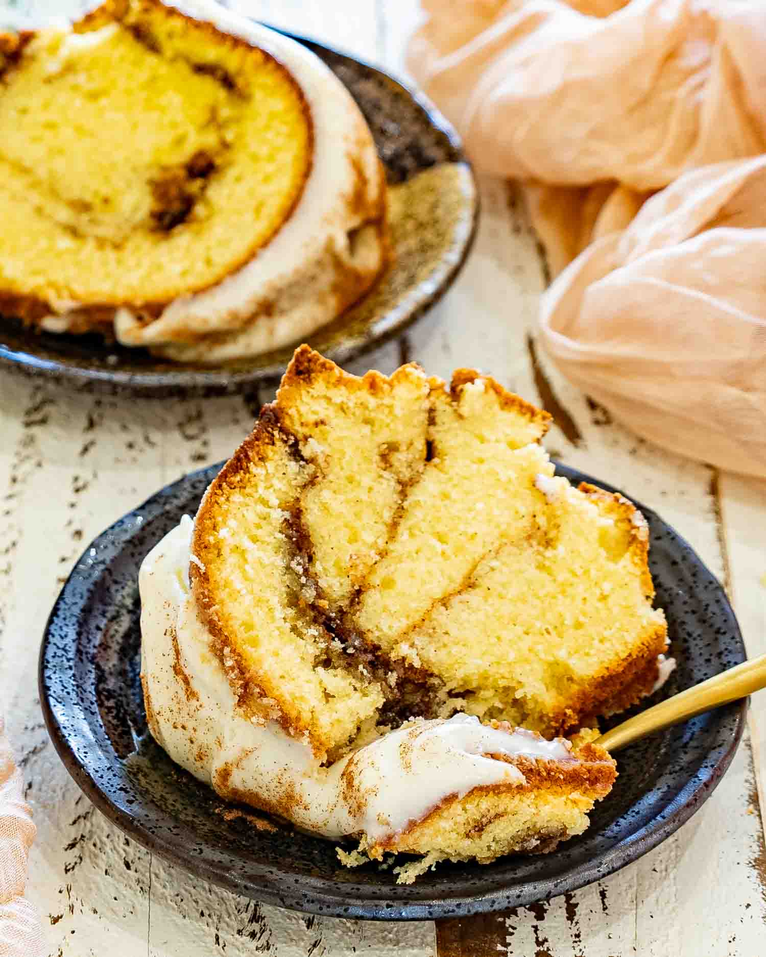 Individual slice of cinnamon roll cream cheese pound cake served with cream cheese frosting, showcasing moist texture and cinnamon ribbon throughout.