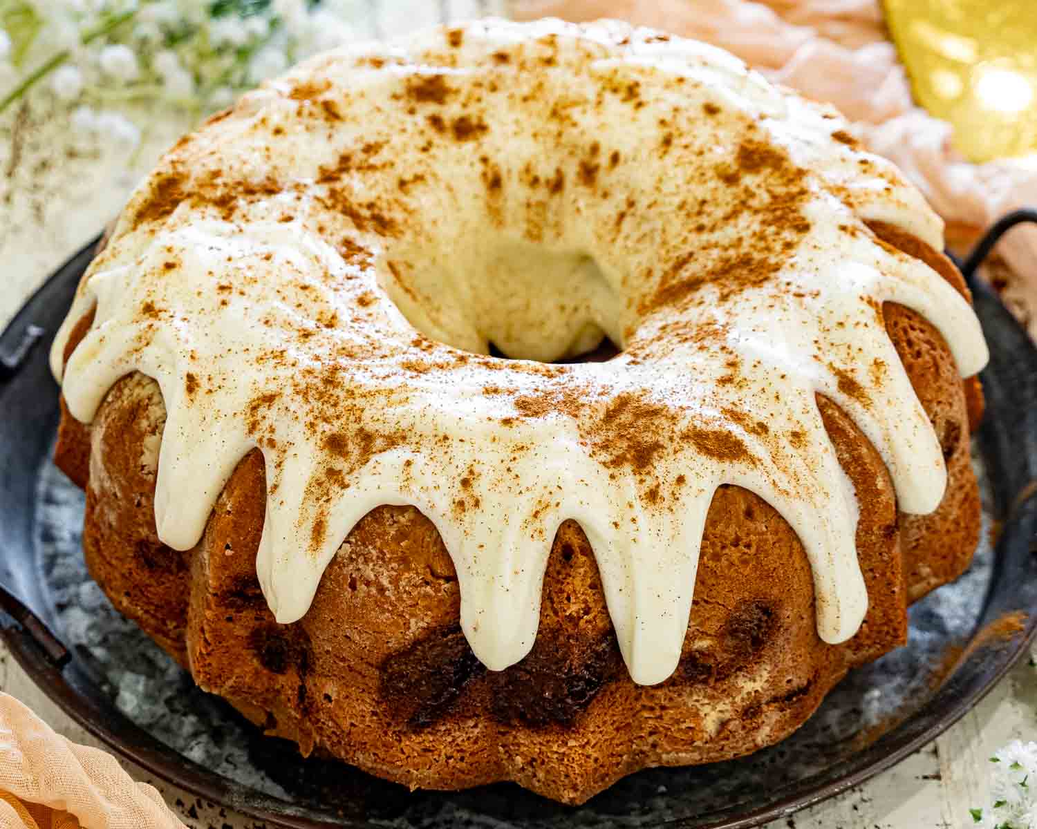 Whole cinnamon roll cream cheese pound cake topped with silky cream cheese glaze and a dusting of cinnamon on a rustic serving platter.