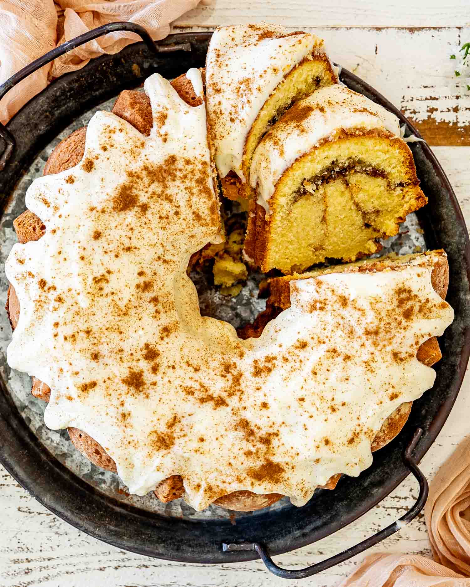 Overhead view of cinnamon roll cream cheese pound cake drizzled with cream cheese glaze, showcasing thick frosting and beautiful cinnamon swirl slices.