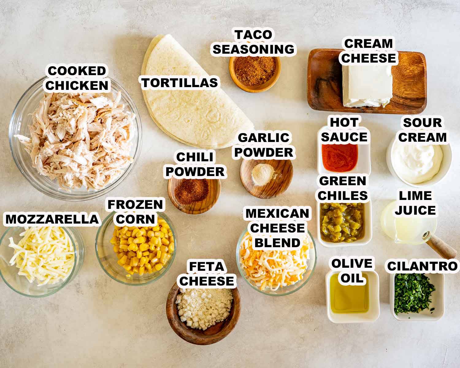 Labeled ingredients for creamy street corn chicken tacos arranged in bowls, including chicken, corn, cheeses, tortillas, seasonings, and sauce.