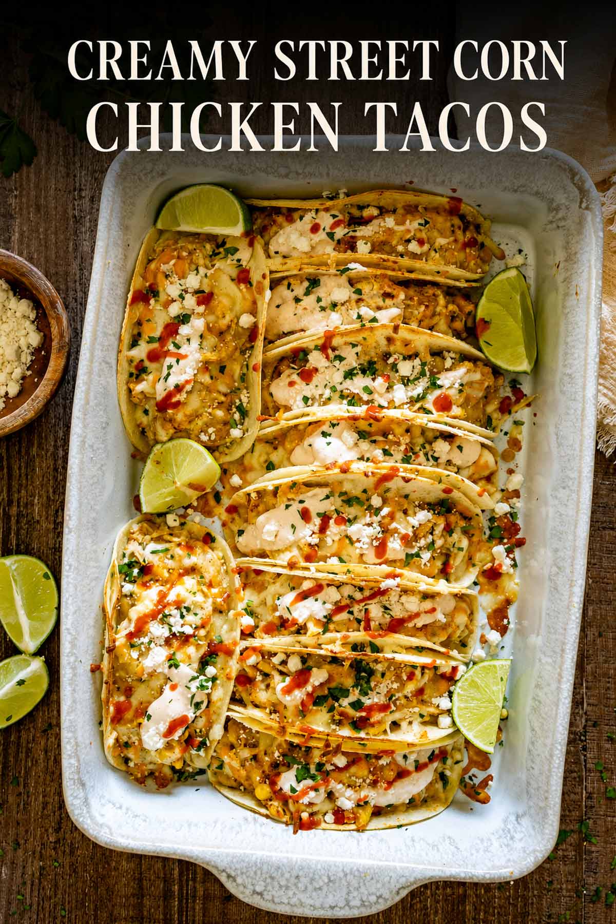 Pinterest graphic showing a baking dish filled with creamy street corn chicken tacos, garnished with feta, cilantro, sauce, and limes.