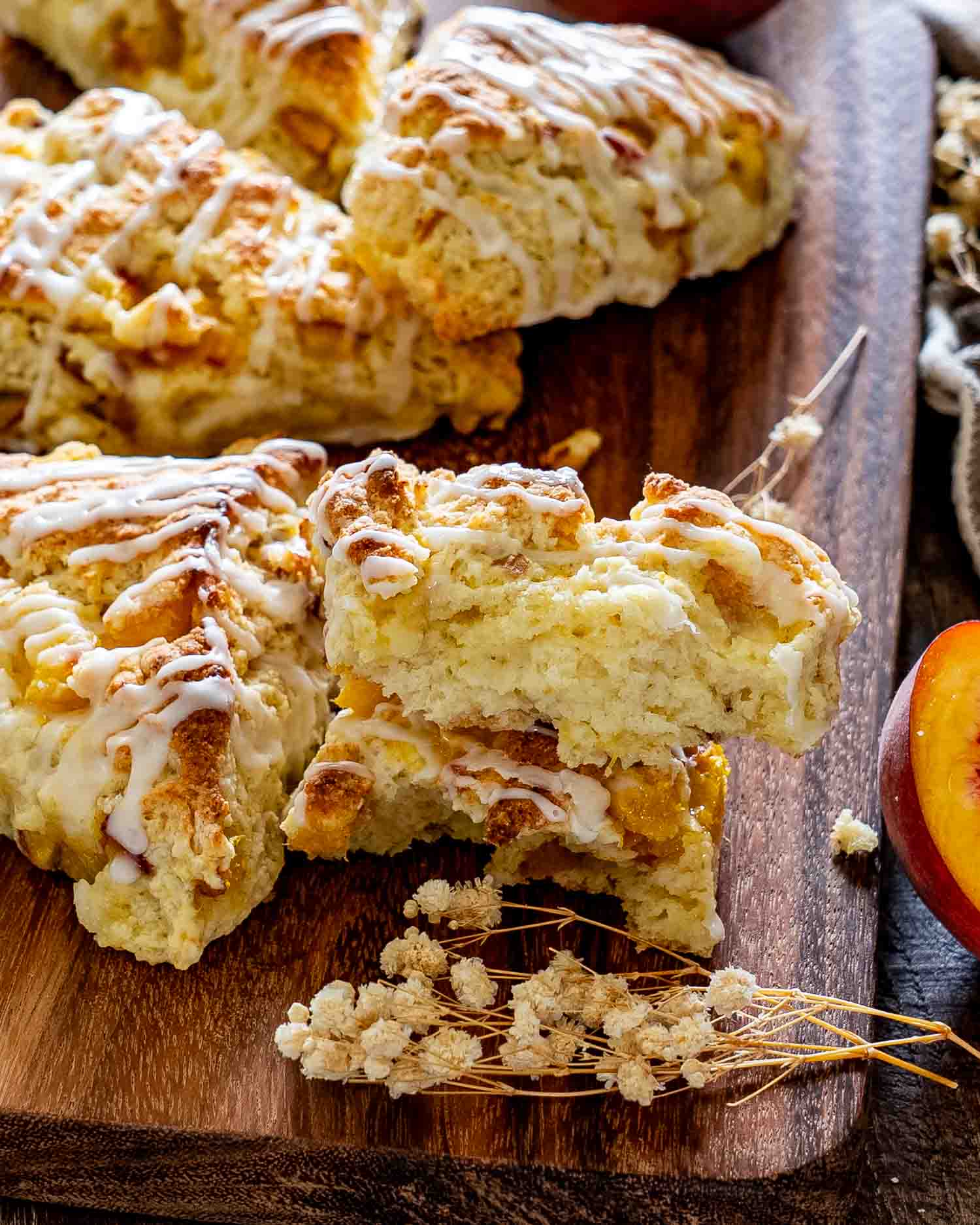 A peach scone split open to reveal its tender, flaky interior, surrounded by glazed scones and fresh peach slices.