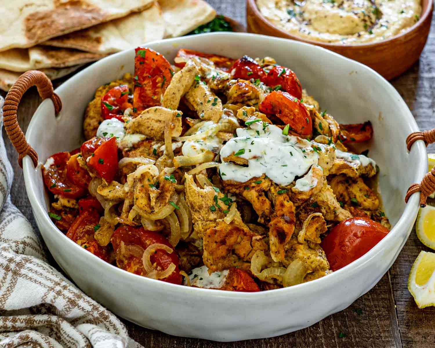 White bowl filled with seasoned chicken shawarma, roasted tomatoes and onions, topped with creamy herb yogurt sauce.