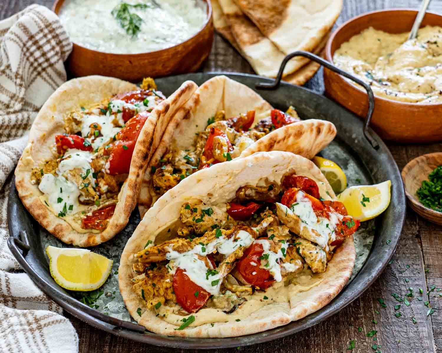 Three warm pita breads filled with chicken shawarma, roasted tomatoes, onions, hummus, herbs, and creamy yogurt sauce.