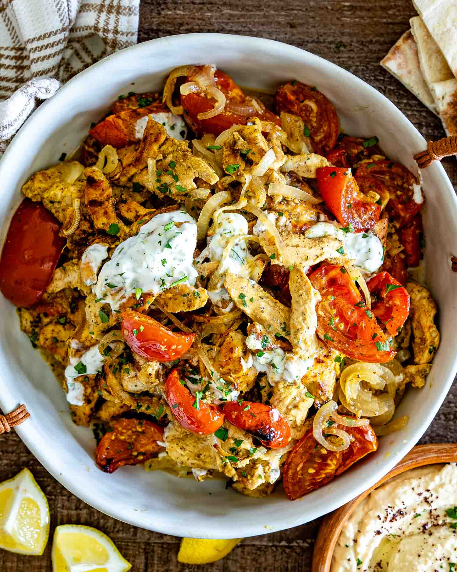 White bowl filled with seasoned chicken shawarma, roasted tomatoes and onions, topped with creamy herb yogurt sauce.