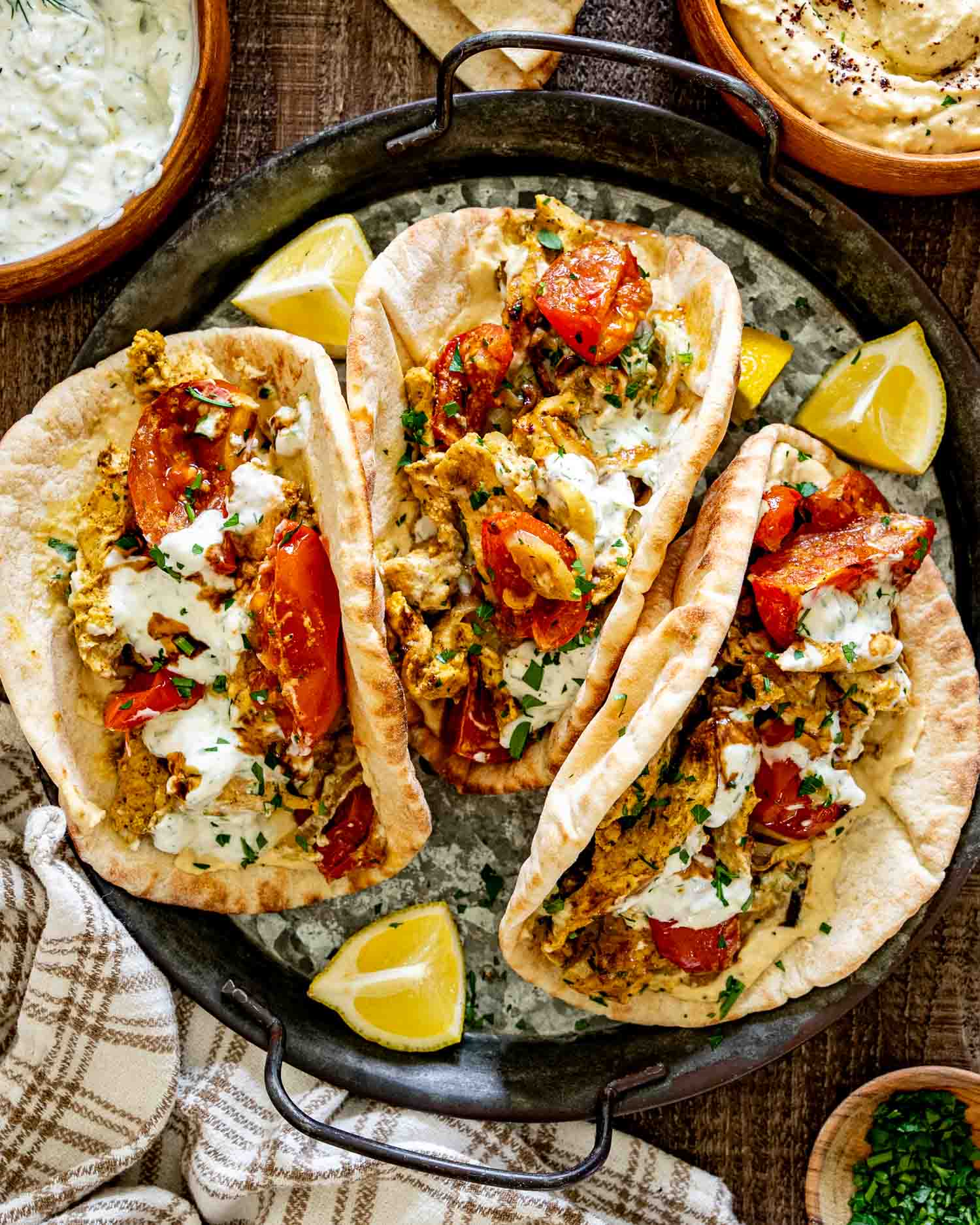 Three warm pita breads filled with chicken shawarma, roasted tomatoes, onions, hummus, herbs, and creamy yogurt sauce.
