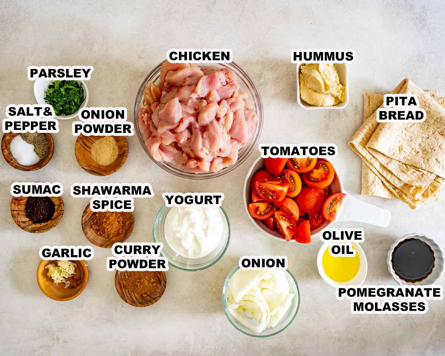 Overhead layout of labeled chicken shawarma ingredients, including spices, yogurt, tomatoes, onion, hummus, pita, and pomegranate molasses.