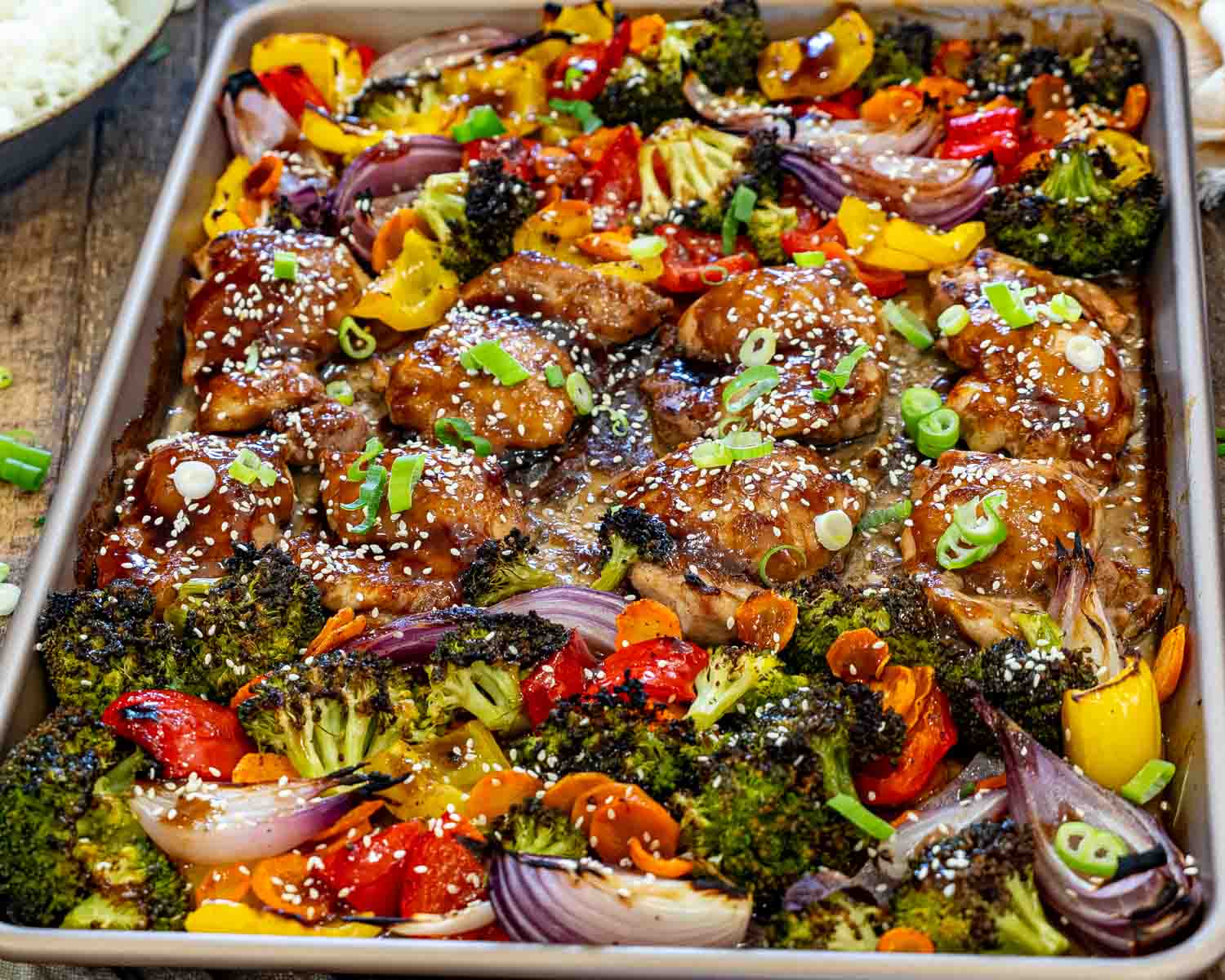 Freshly baked sheet pan teriyaki chicken surrounded by caramelized broccoli, peppers, carrots, and red onion, finished with sesame seeds.