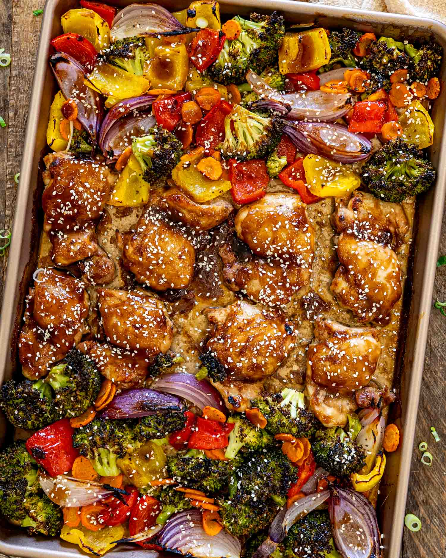 Overhead view of sheet pan teriyaki chicken glazed with teriyaki sauce, surrounded by colorful roasted vegetables and sesame seed garnish.