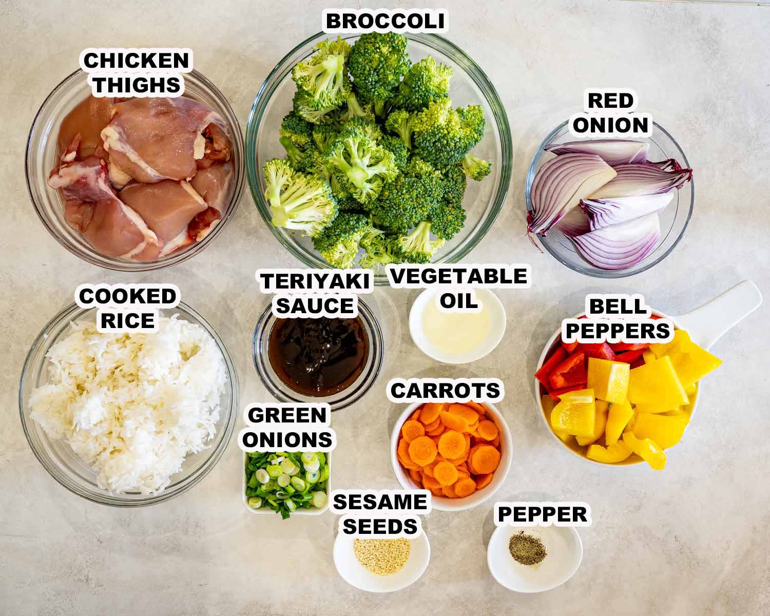 Overhead view of sheet pan teriyaki chicken ingredients including chicken thighs, broccoli, peppers, carrots, onions, rice, and teriyaki sauce.