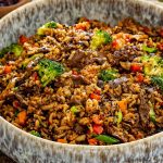 Close-up of sticky beef fried rice packed with tender beef, crisp broccoli, mushrooms, peppers, carrots, and savory seasoned rice.