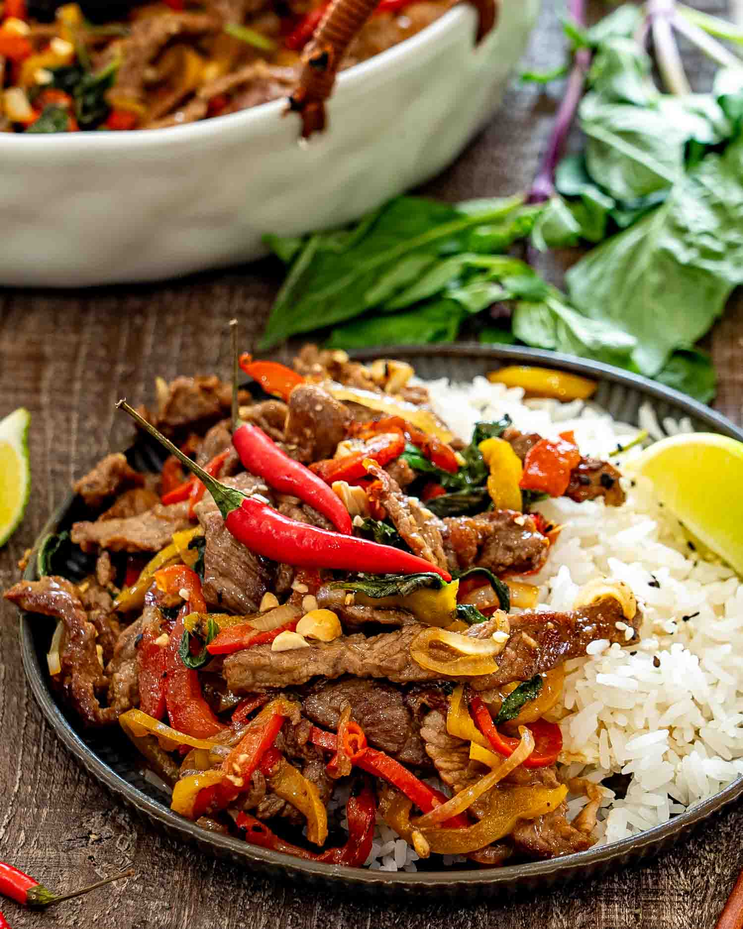 Thai basil beef with peppers and chilies is served beside fluffy white rice, chopped peanuts, and fresh lime.
