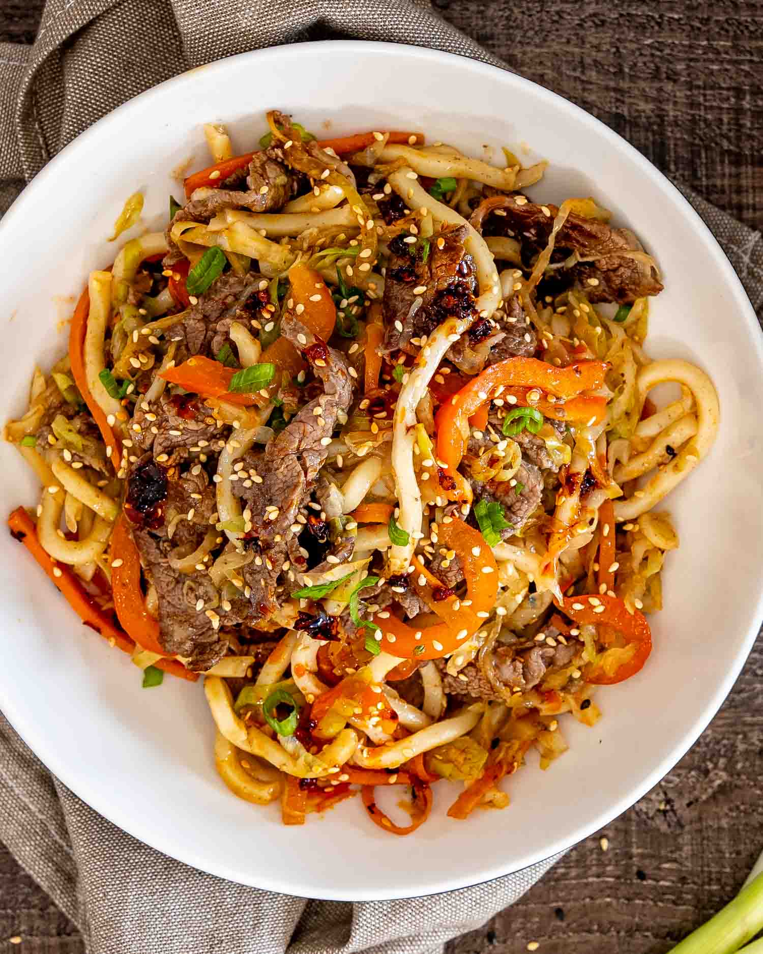 Overhead close view of beef yaki udon topped with sesame seeds and green onions in a white bowl.