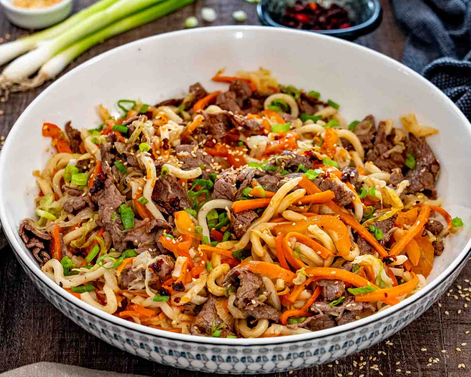Close view of beef yaki udon in a patterned serving bowl with carrots, bell peppers, cabbage, and green onions.