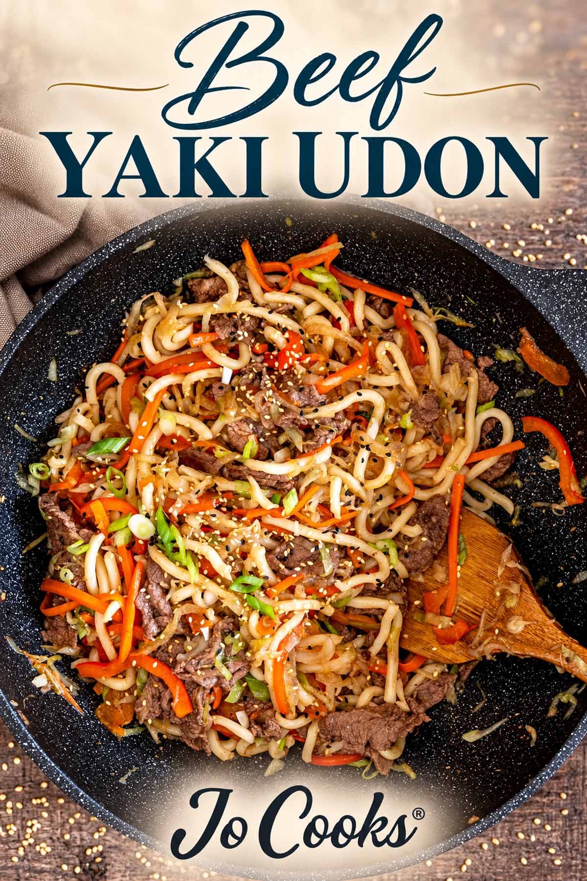 Beef yaki udon in a black wok with vegetables, topped by the recipe title and Jo Cooks logo below.