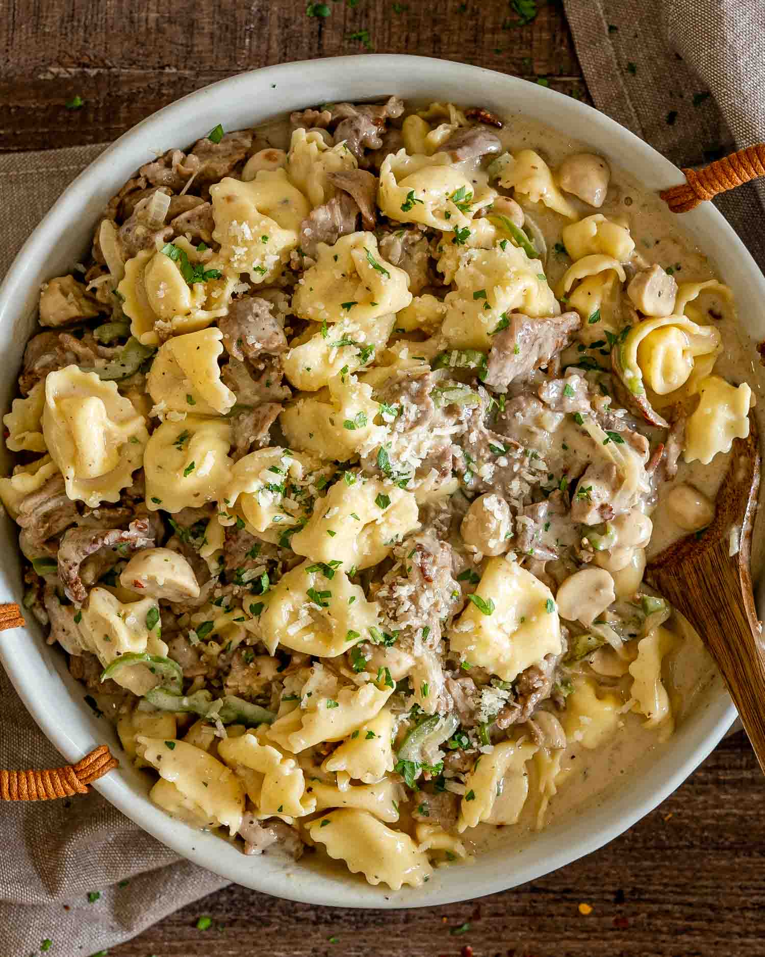 Overhead view of cheesesteak tortellini with sliced steak, mushrooms, peppers, Parmesan, and parsley in creamy sauce.