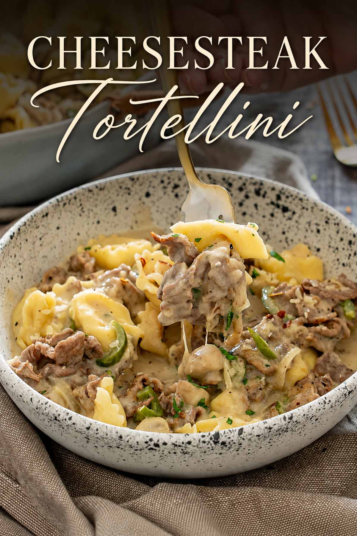 Pinterest image of creamy cheesesteak tortellini with steak and mushrooms, featuring a fork lifting a cheesy bite.