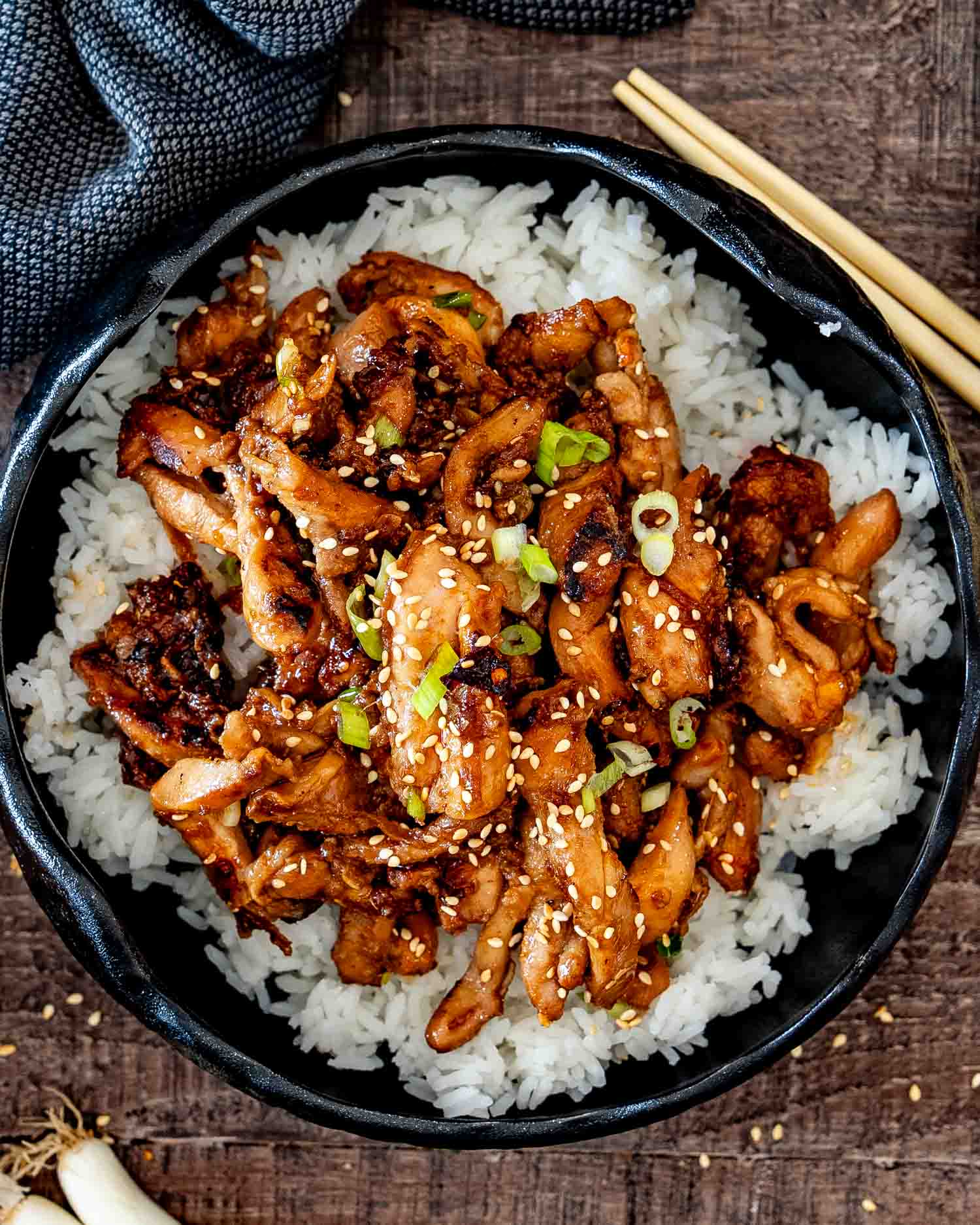 Overhead view of chicken bulgogi arranged over steamed white rice in a black skillet with chopsticks nearby.