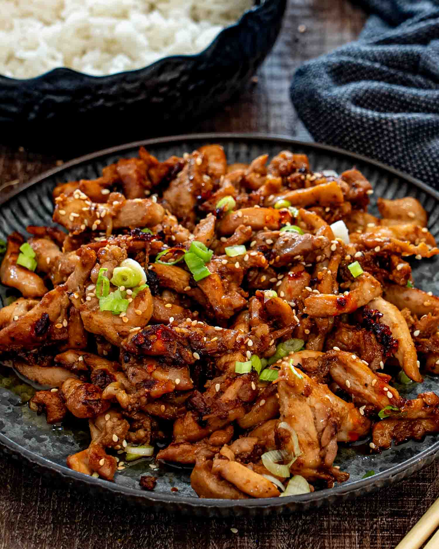Close-up platter of glossy chicken bulgogi with charred edges, sprinkled with sesame seeds and chopped green onions.