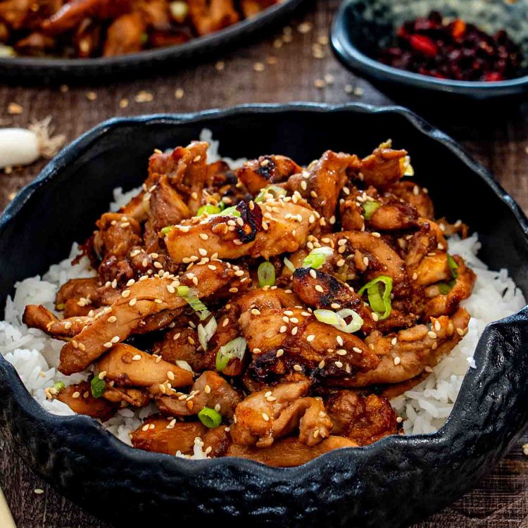 Close-up hero shot of caramelized chicken bulgogi over rice, finished with sesame seeds and fresh green onions.