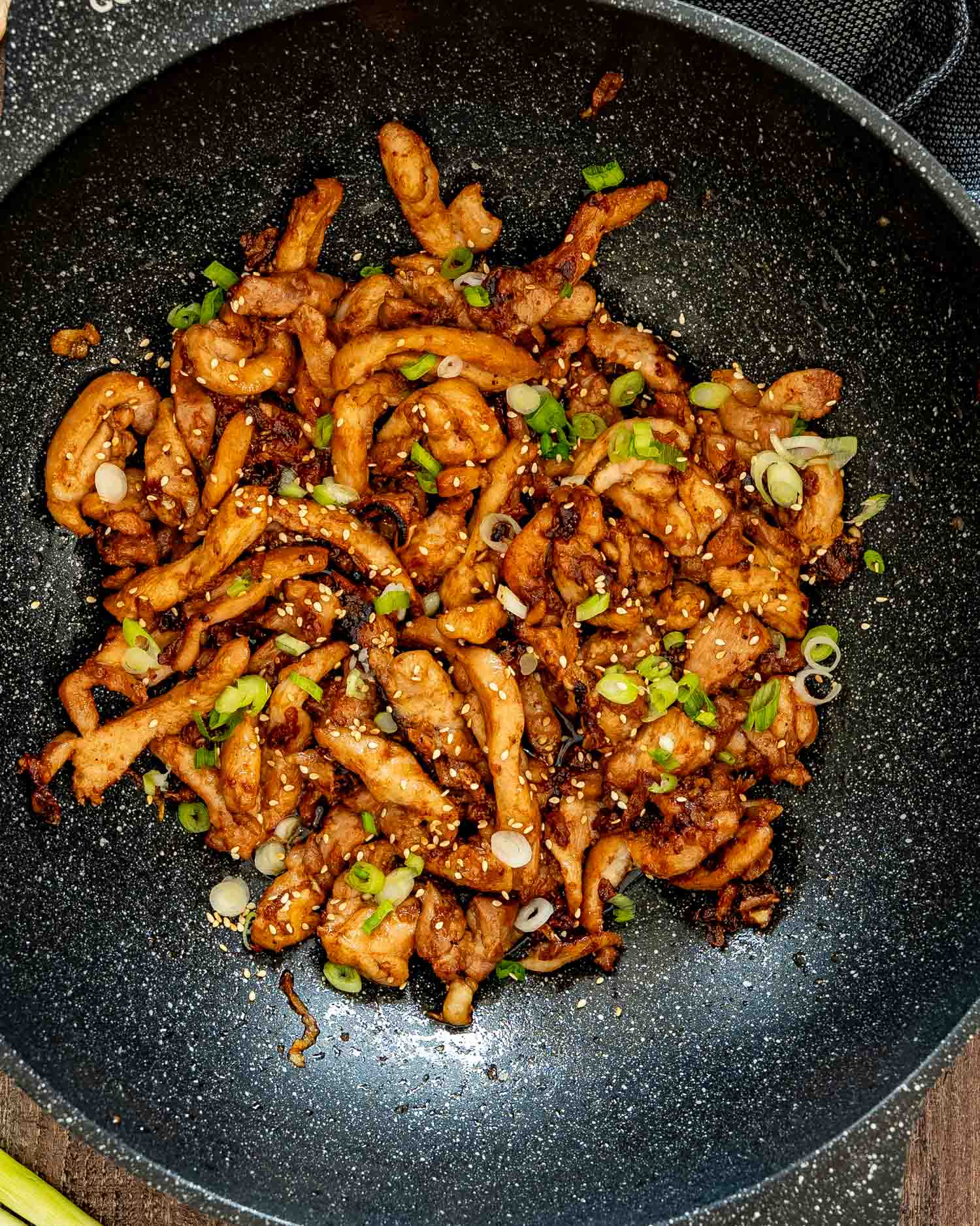 Cooked chicken bulgogi rests in a skillet with charred edges, sesame seeds, and bright sliced green onions.