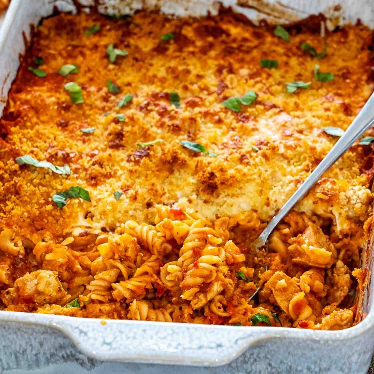 Chicken Parmesan casserole in a white baking dish, showing saucy rotini and chicken beneath its crisp golden topping.