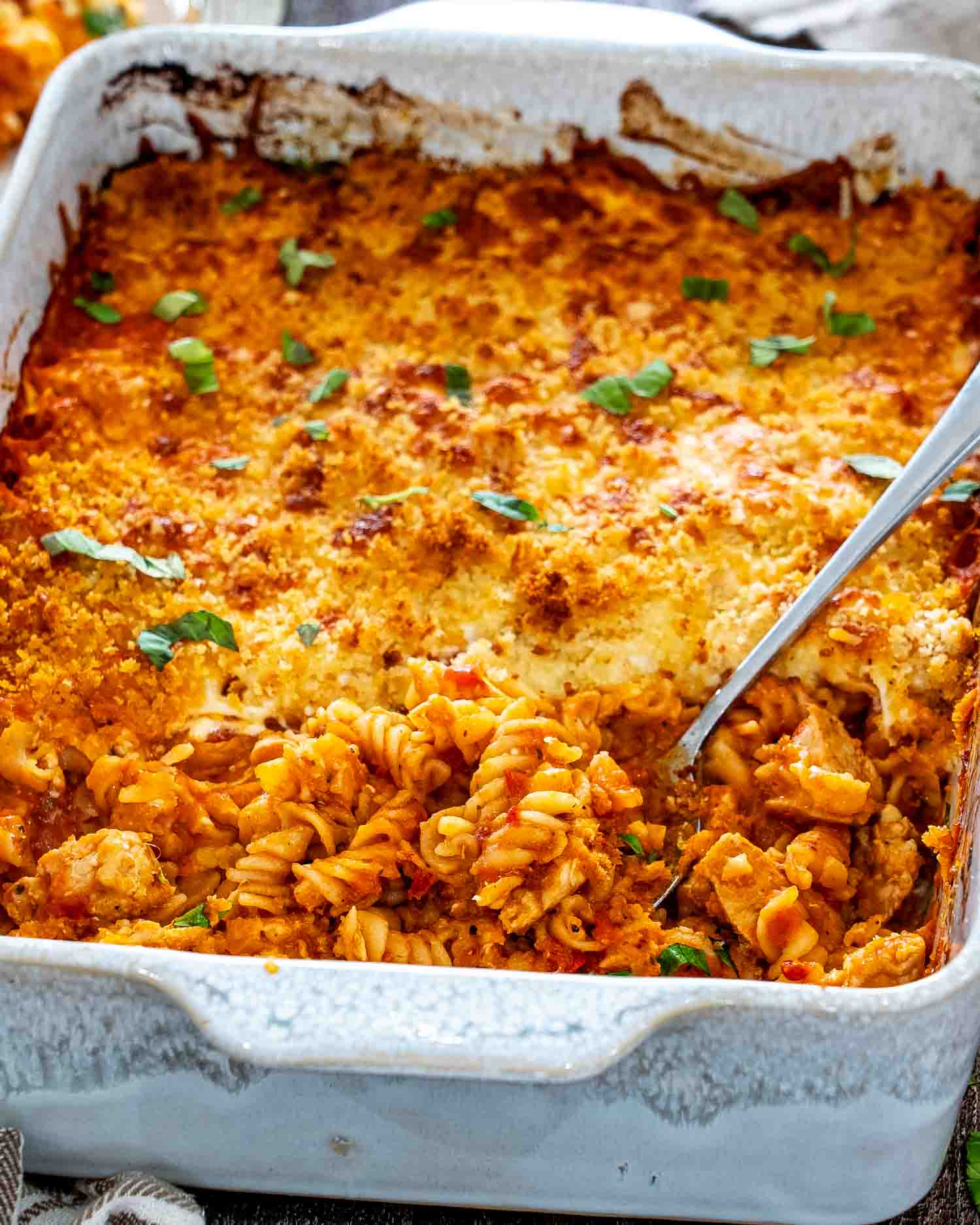 Chicken Parmesan casserole in a white baking dish, showing saucy rotini and chicken beneath its crisp golden topping.