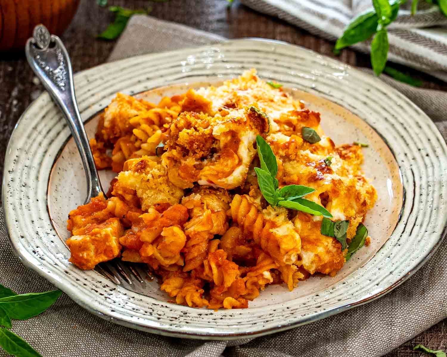Chicken Parmesan casserole served on a rustic plate with saucy rotini, melted mozzarella, crisp breadcrumbs, and fresh basil.