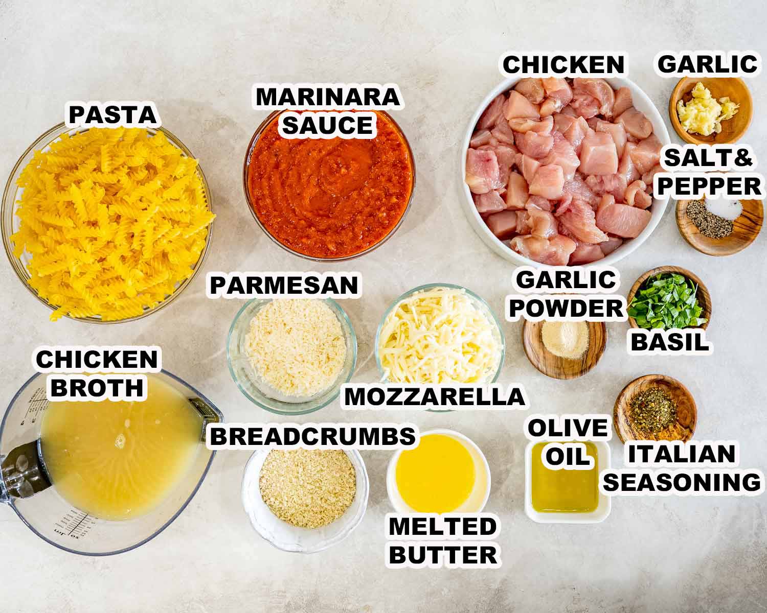Overhead display of labeled ingredients for chicken Parmesan casserole, including pasta, chicken, marinara, cheeses, breadcrumbs, seasonings, and broth.