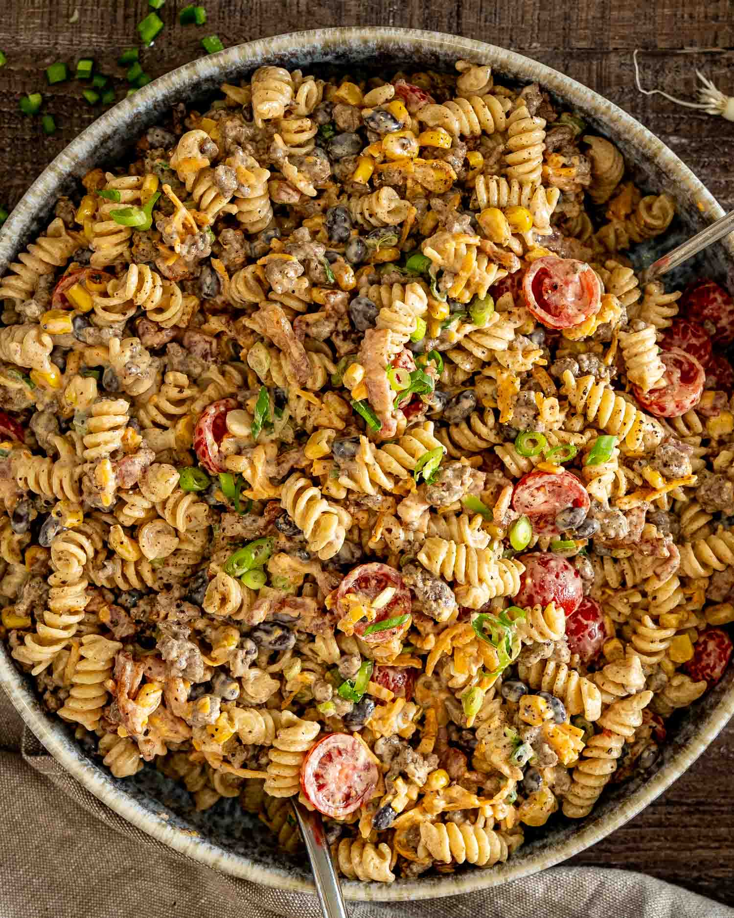 Large bowl filled with creamy cowboy pasta salad featuring seasoned beef, bacon, black beans, corn, tomatoes, and cheddar.