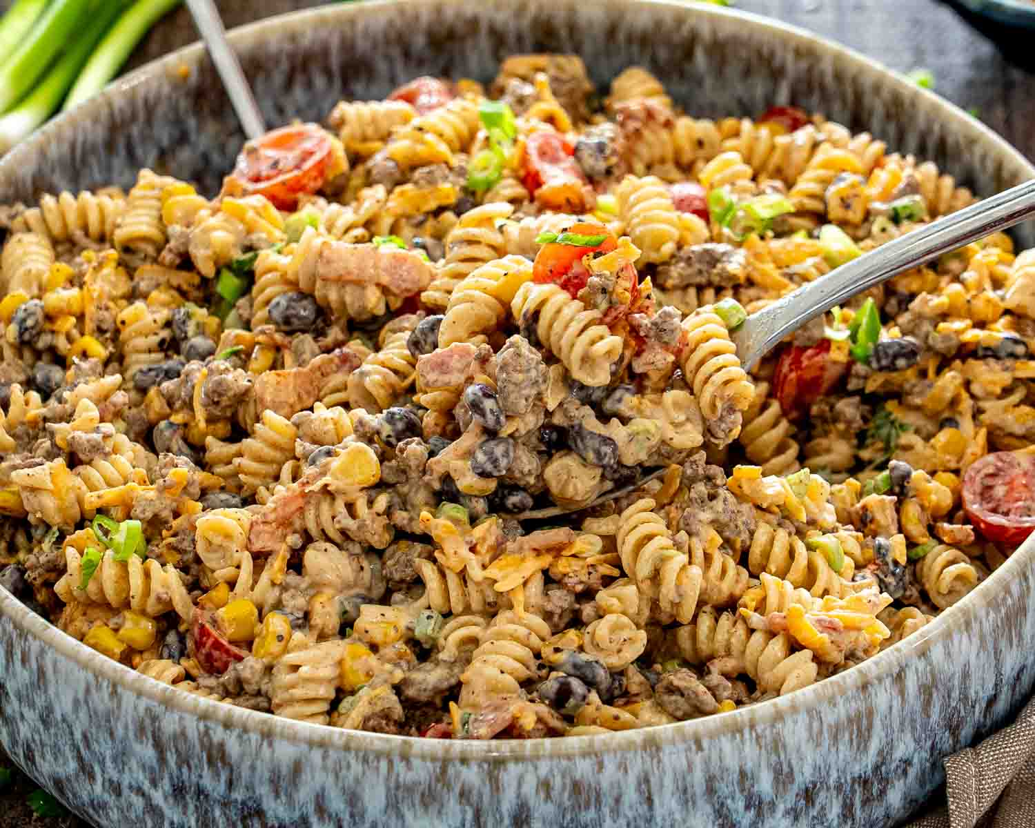 Close-up of creamy cowboy pasta salad with a spoonful of rotini, beef, bacon, black beans, corn, and tomatoes.