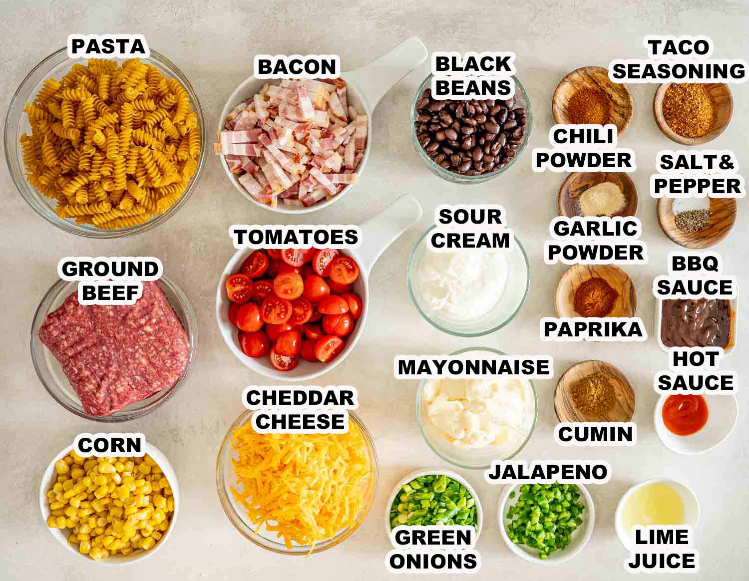 Labeled cowboy pasta salad ingredients arranged overhead, including rotini, beef, bacon, vegetables, cheese, dressing ingredients, and seasonings.