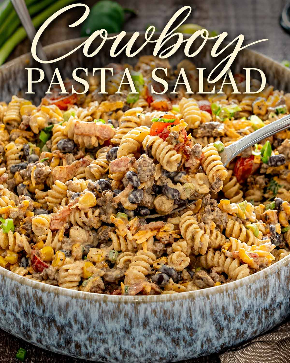 Creamy cowboy pasta salad with beef, bacon, corn, beans, tomatoes, and cheddar beneath an elegant recipe title.