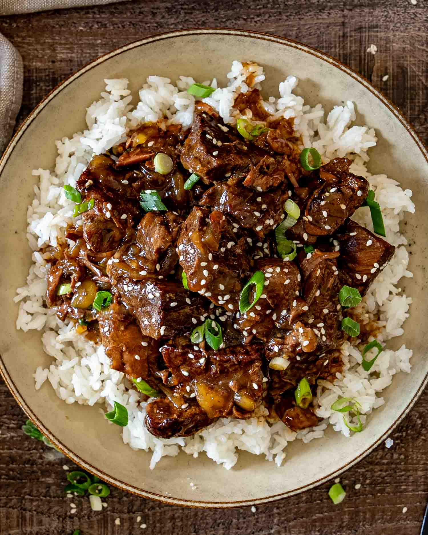 Asian braised beef served over fluffy white rice with glossy sauce, sesame seeds, and fresh sliced green onions.