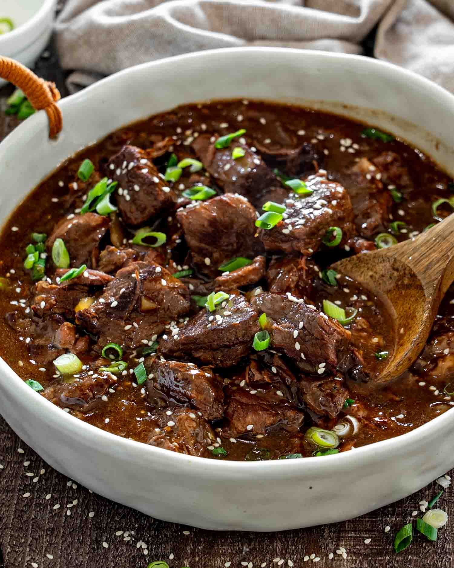 Slow cooker Asian braised beef chunks in a rich glossy sauce, topped with sesame seeds and sliced green onions.