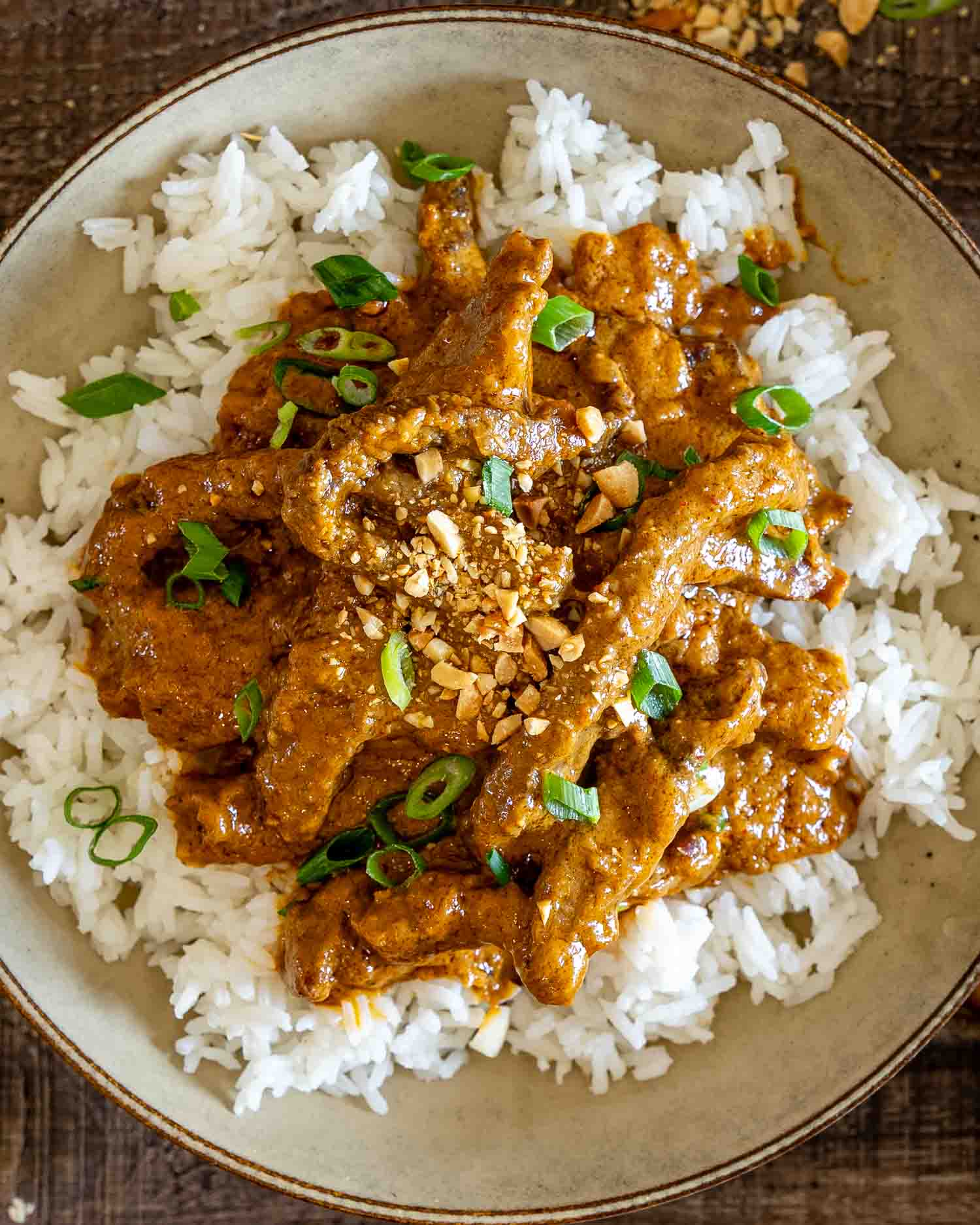 Bowl of curried beef in creamy peanut sauce served over white rice with chopped peanuts and green onions.