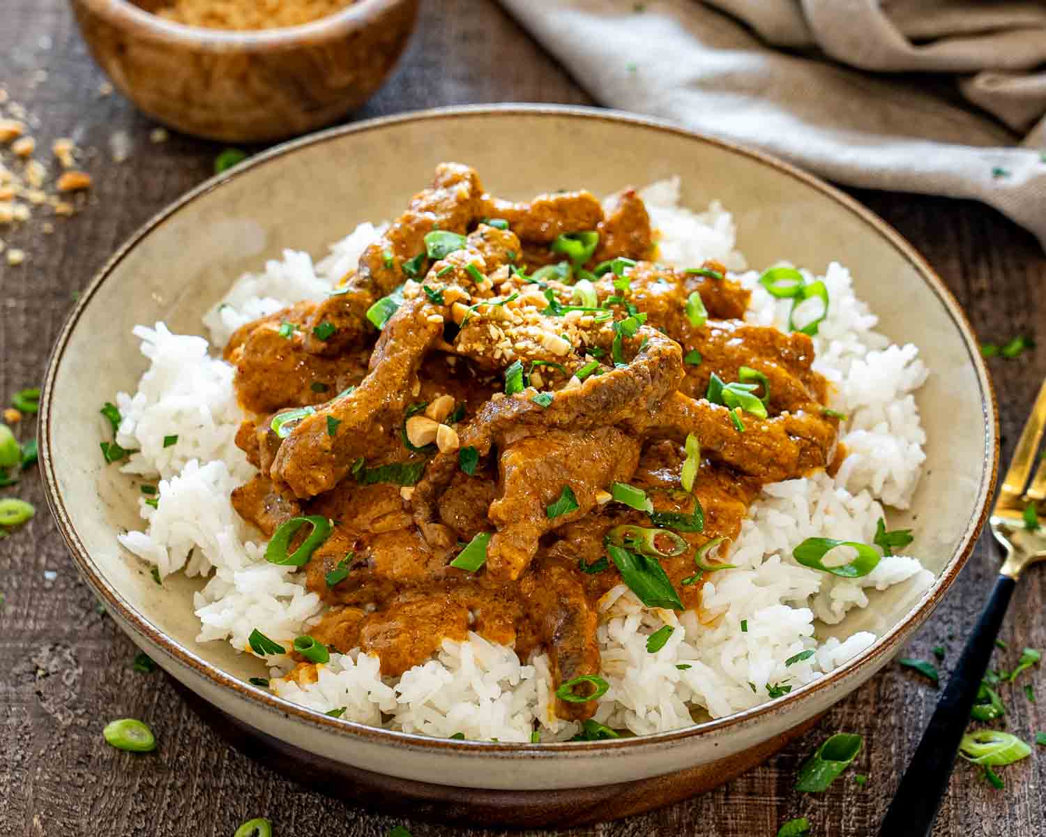 Curried beef with creamy peanut sauce served over fluffy white rice, topped with peanuts, herbs, and green onions.