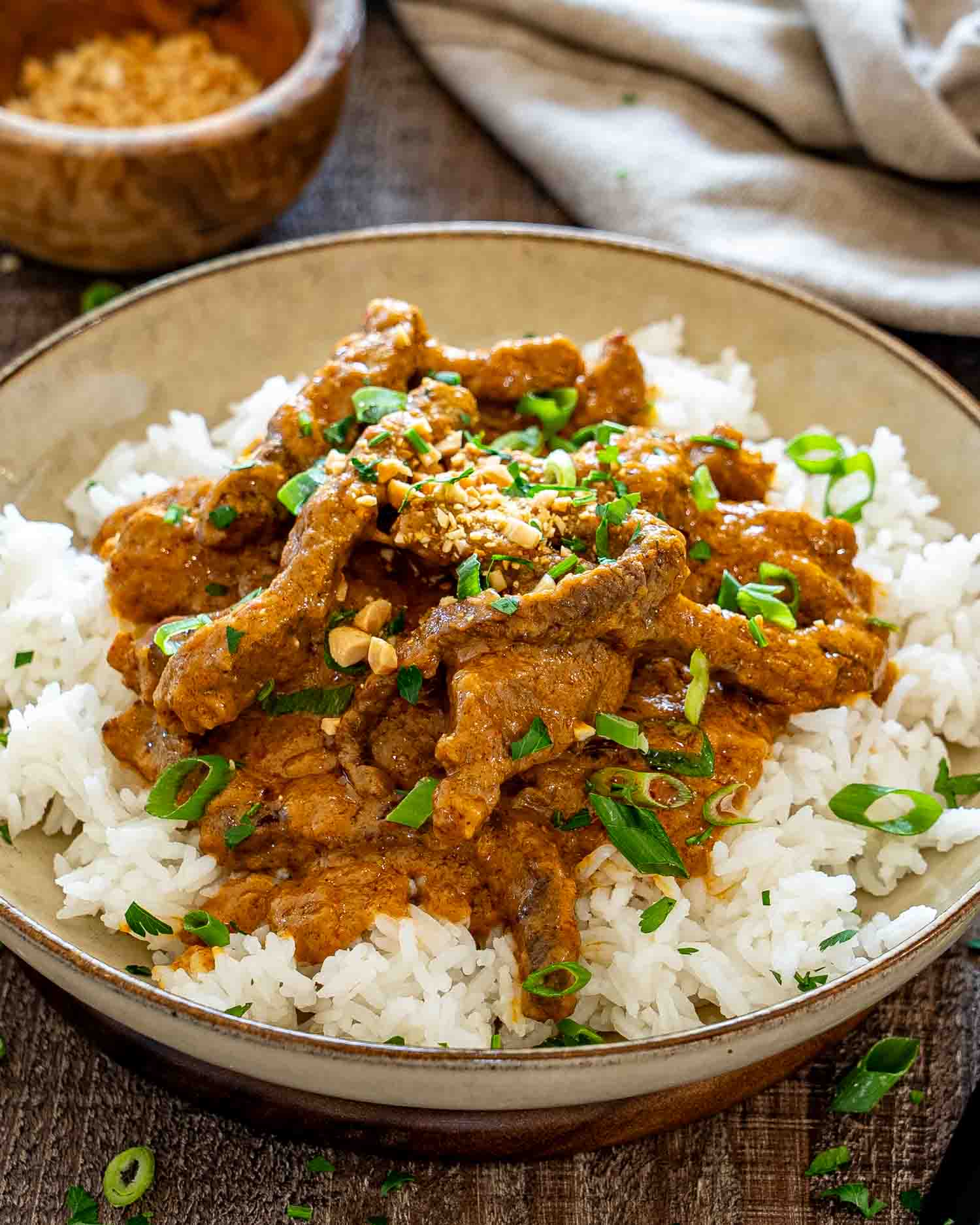 Tender curried beef strips coated in creamy peanut sauce over white rice with chopped peanuts and scallions.