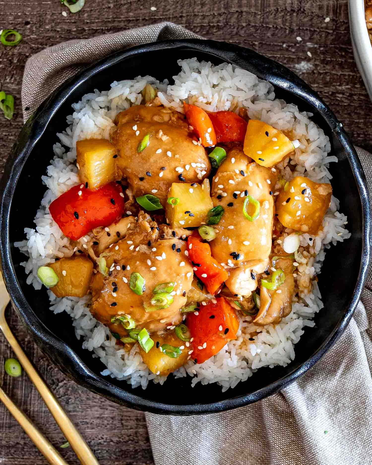 Hawaiian chicken thighs, pineapple, and red peppers served over fluffy white rice in a rustic black bowl.