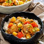 Close-up of glazed Hawaiian chicken, pineapple, and red peppers served over rice and garnished with green onions and sesame seeds.