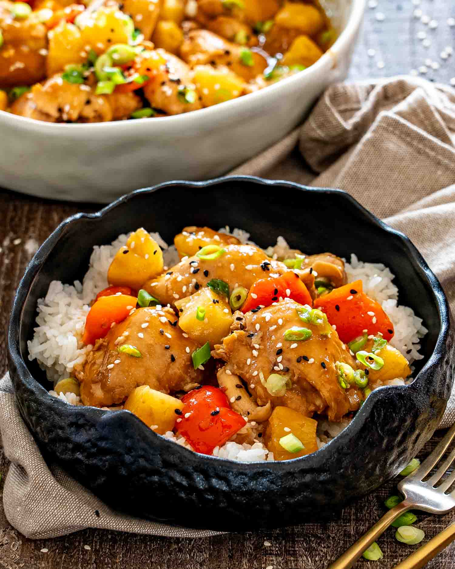 Close-up of glazed Hawaiian chicken, pineapple, and red peppers served over rice and garnished with green onions and sesame seeds.